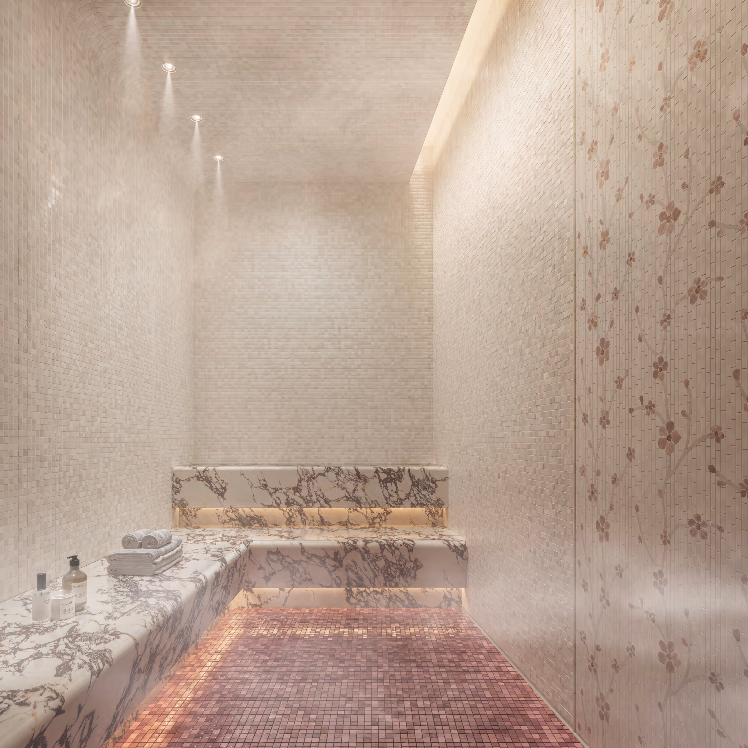 Marble bench with towels and spa products in a softly lit mosaic-tiled steam room with floral wall tiles.