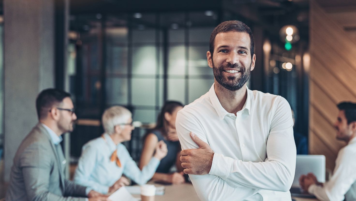 Homme souriant en chemise blanche dans un espace de coworking moderne avec une équipe en arrière-plan