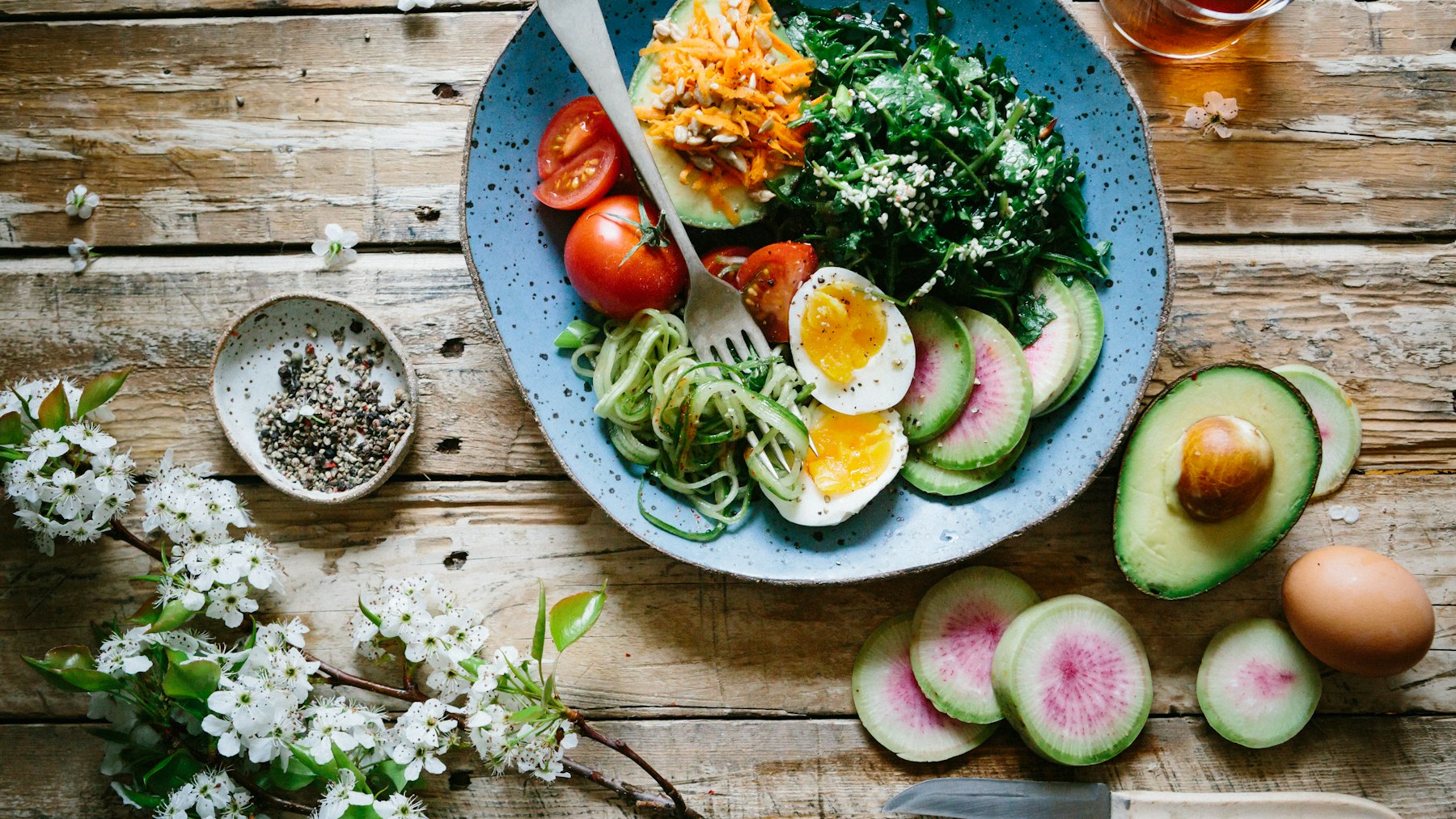 A plate of eggs, avocado, tomatoes and leafy greens on a wooden table
