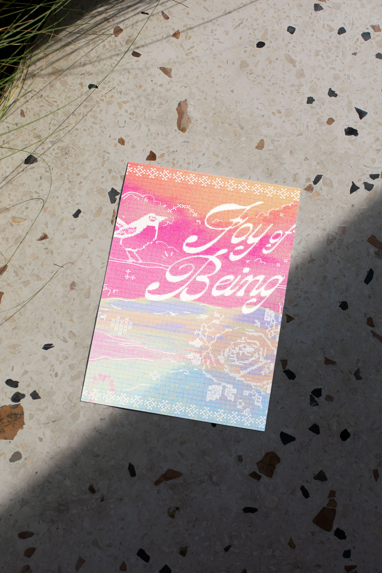 A print that is mainly in baby blue and a vivid orange and pink touch, that says "Joy of Being", with cross stitching illustrations of a rose, a sparrow standing on a stick, and cross-stitching borders on the top and the bottom as borders on the print.