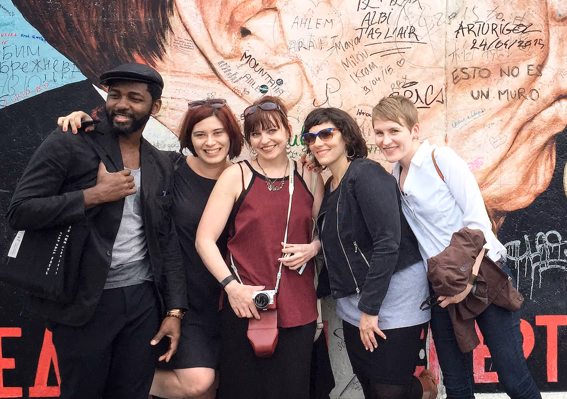 Five IDSVA students posing together in front of a graffiti-covered mural wall