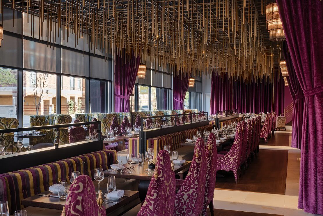 A dining room with purple curtains and a chandelier.