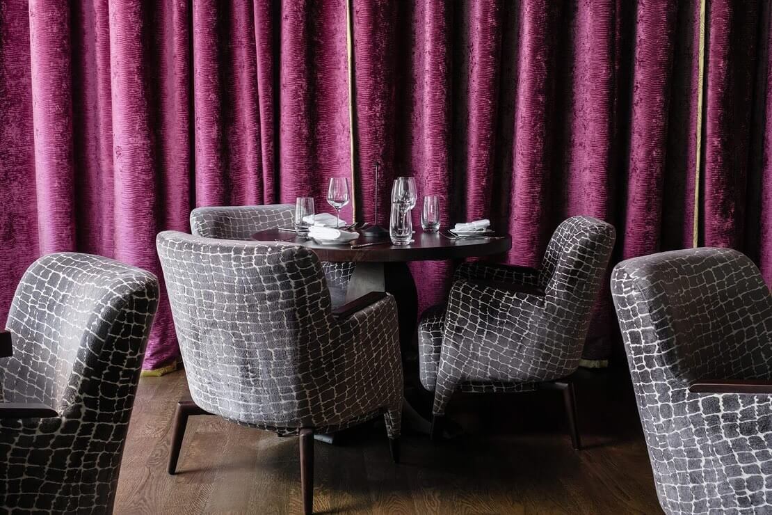 A dining room with purple curtains and chairs.