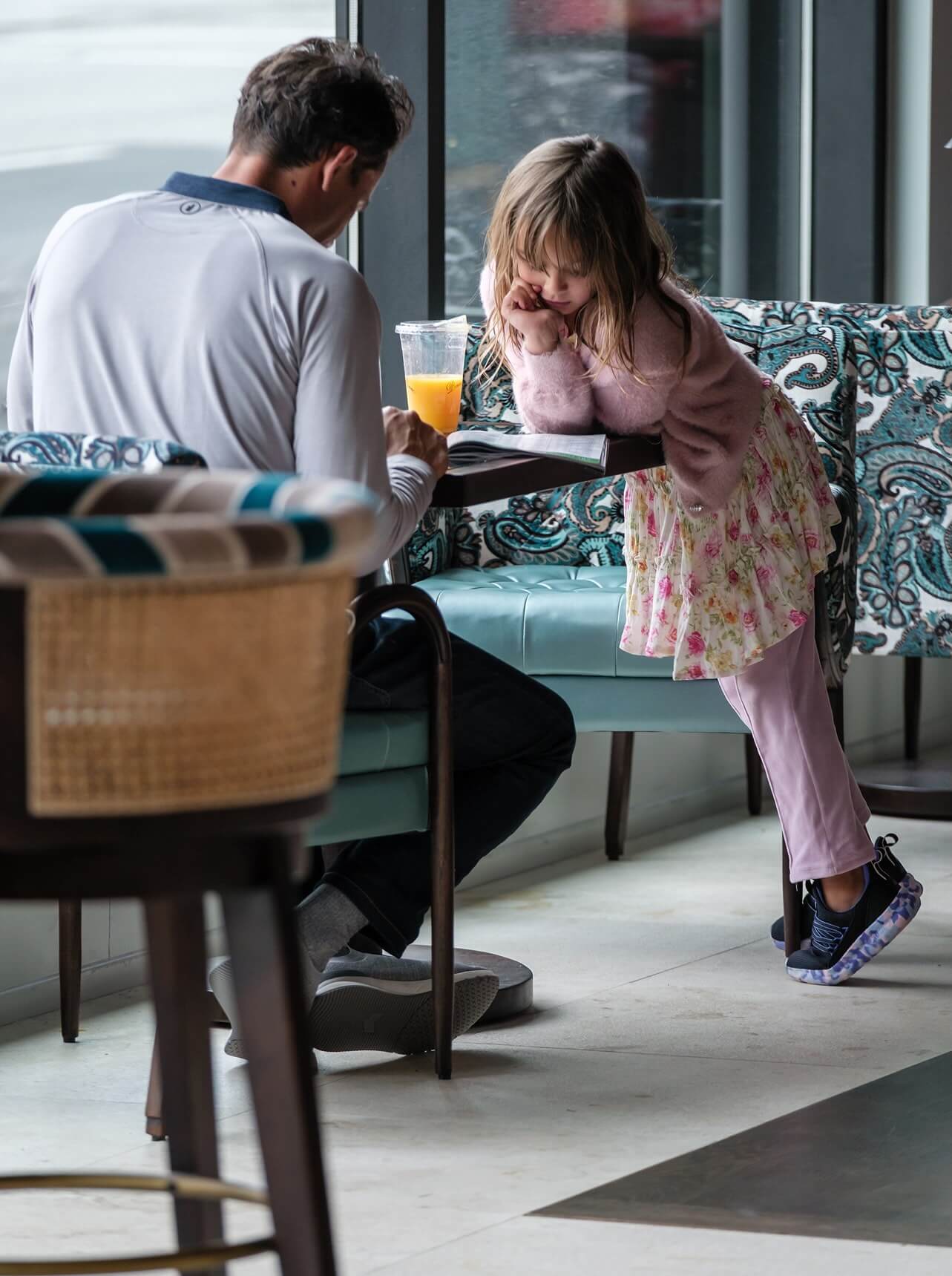 A little girl sitting at a table with a glass of orange juice.