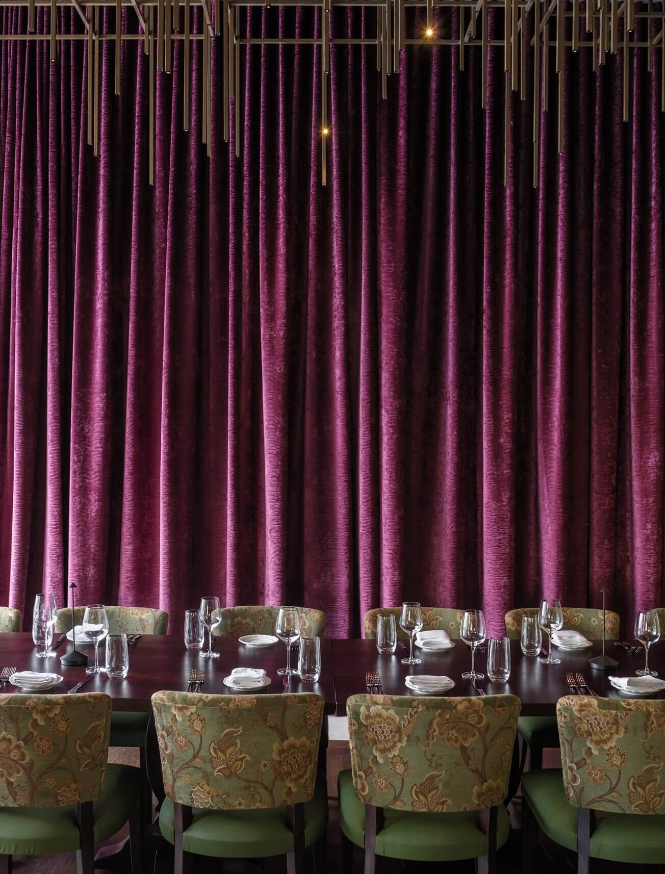 A dining room with a purple curtain and green chairs.