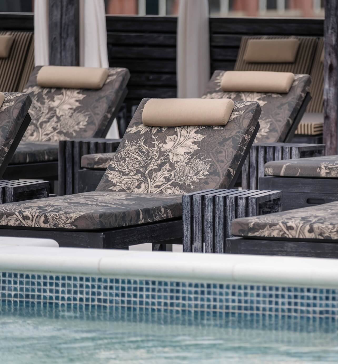 A row of lounge chairs next to a swimming pool.