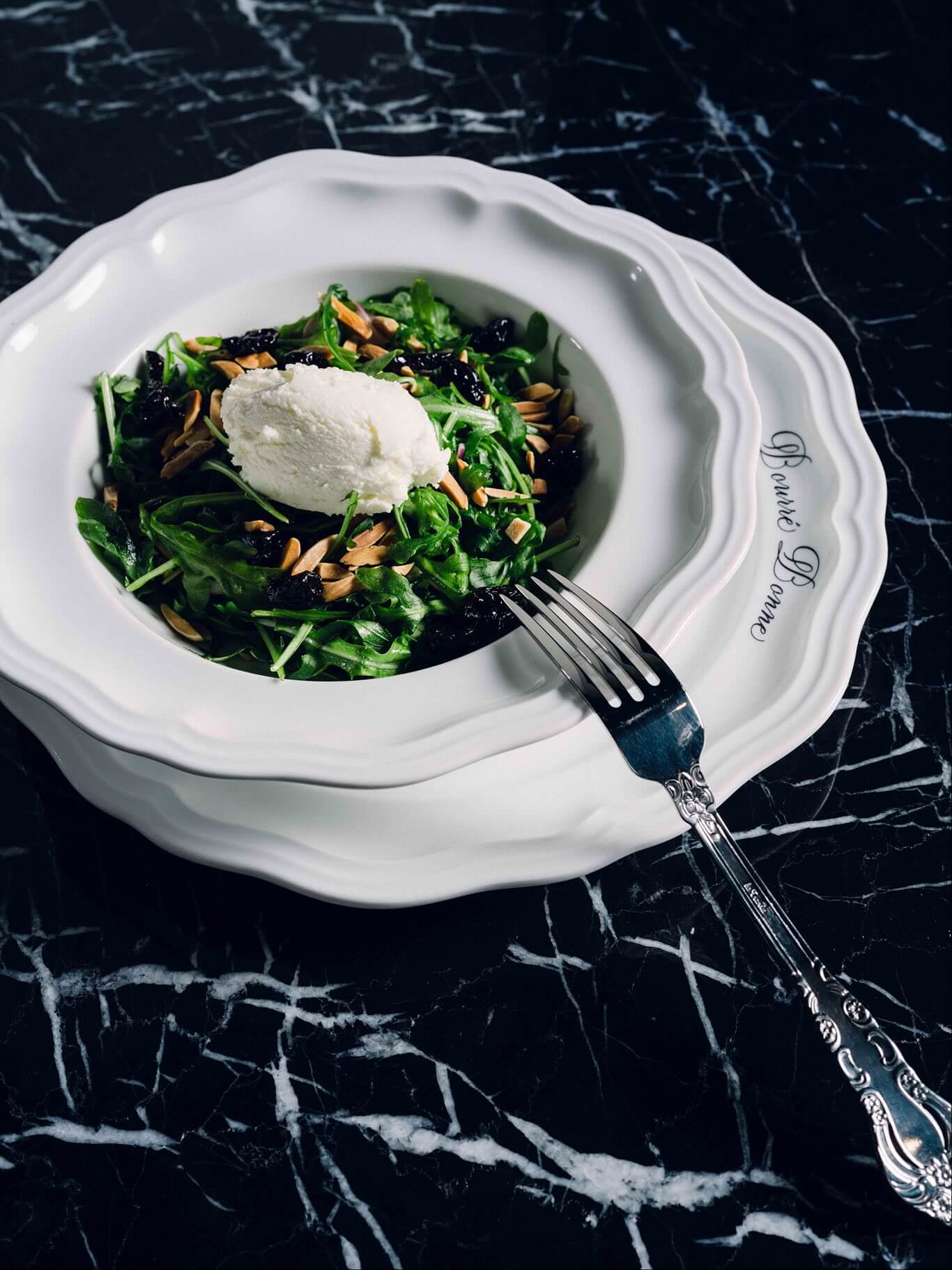 A white bowl filled with a salad and a fork.