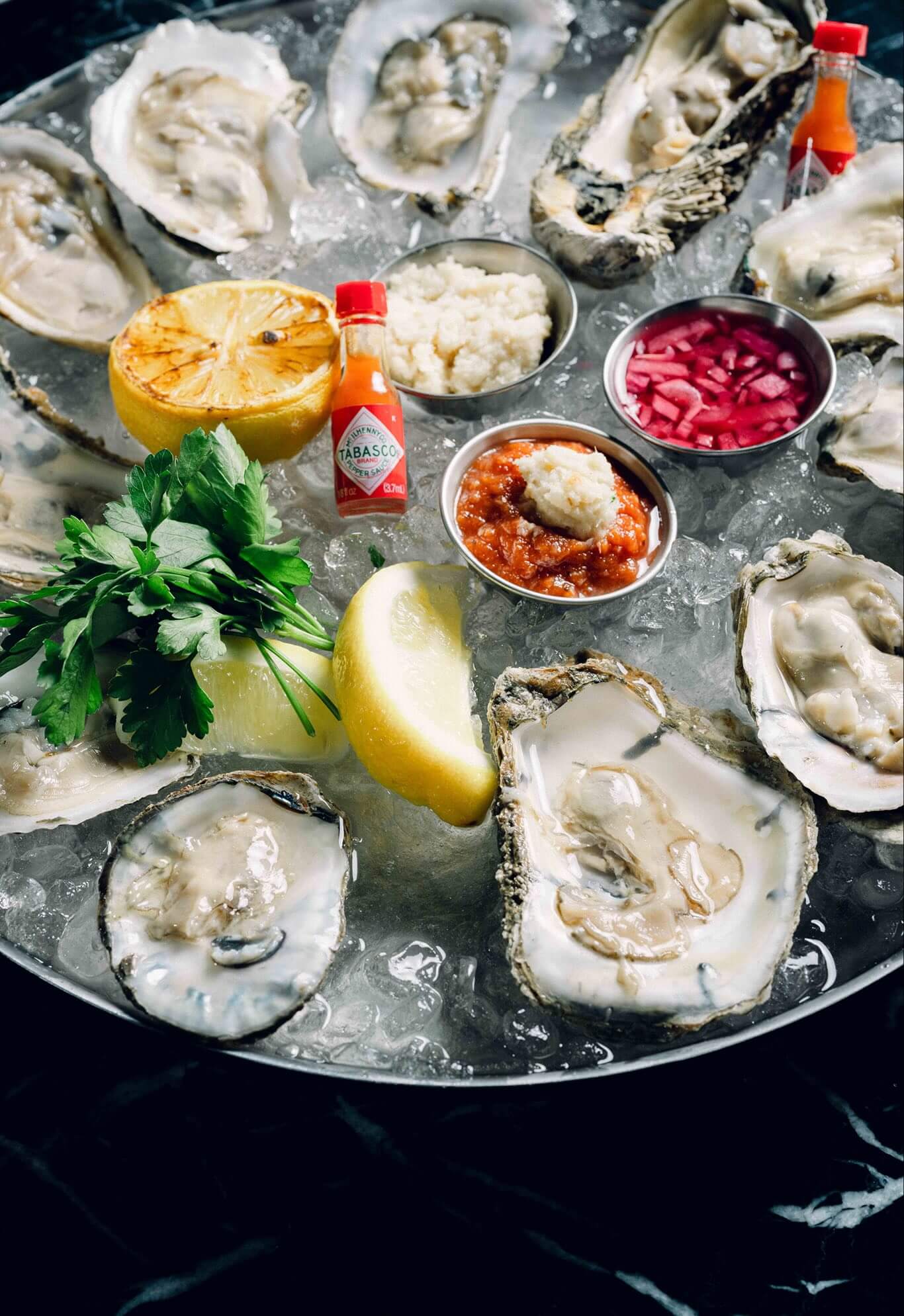 A platter of oysters with a lemon wedge and sauce.