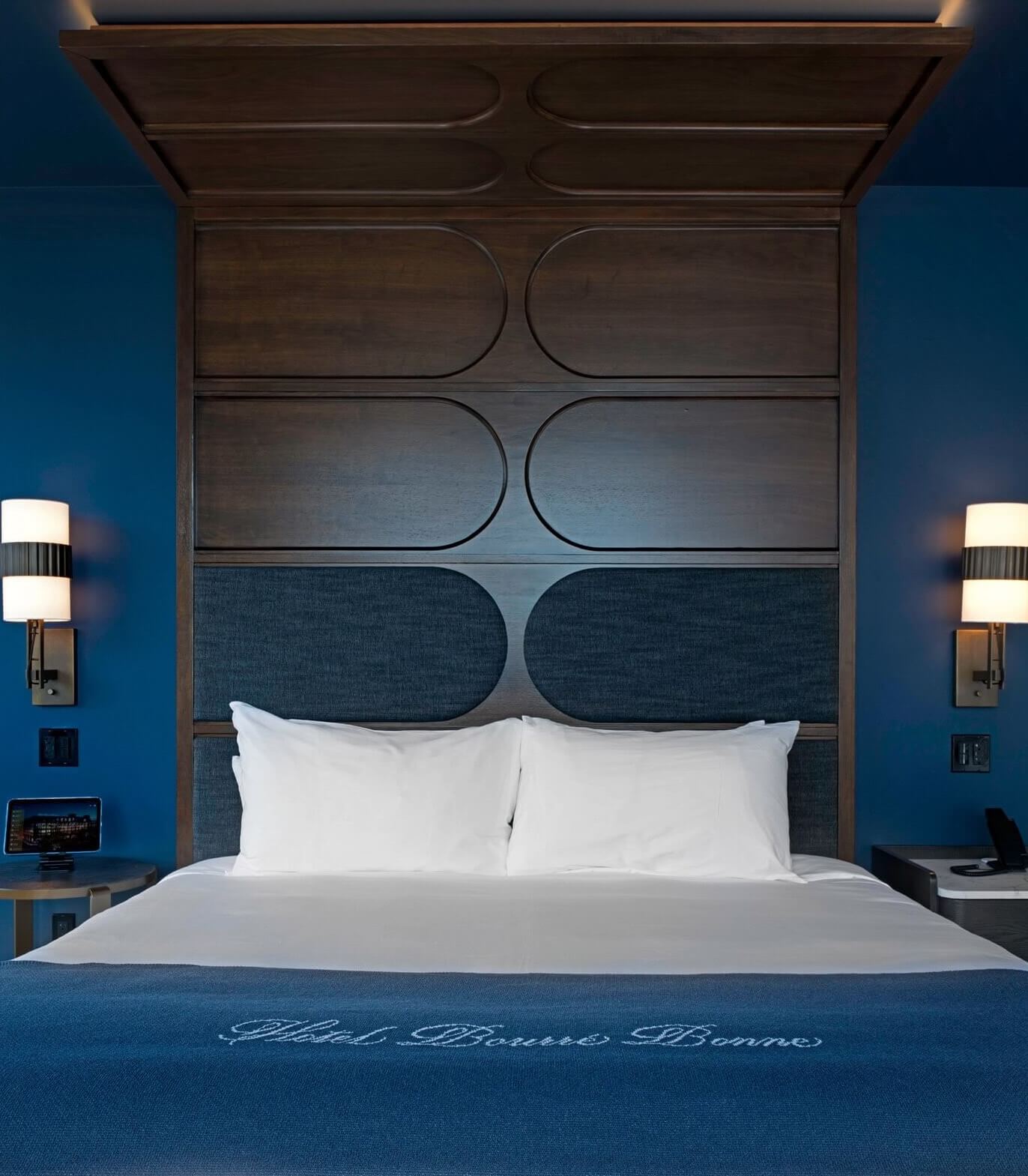 A bed with a blue headboard and two lamps.
