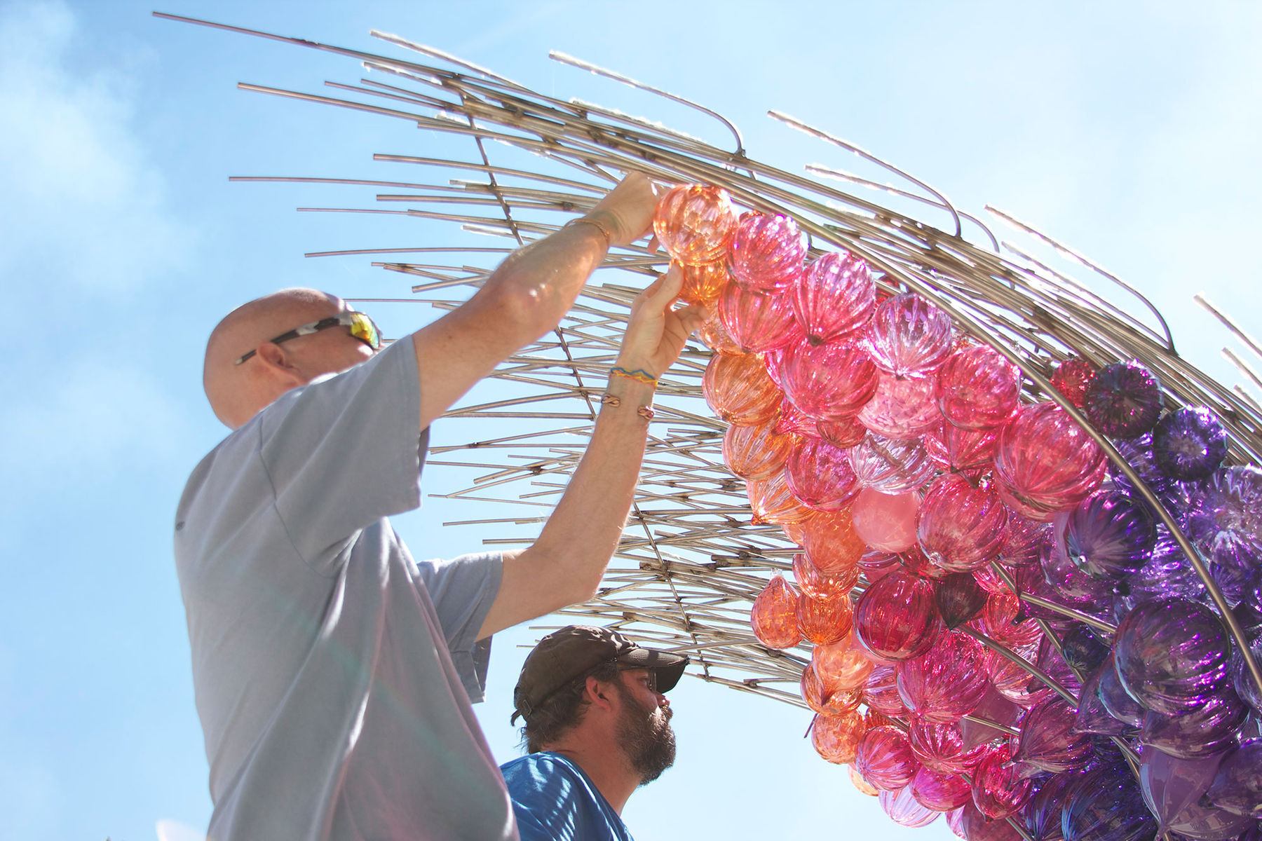 A man standing next to a man holding a bunch of glass beads.