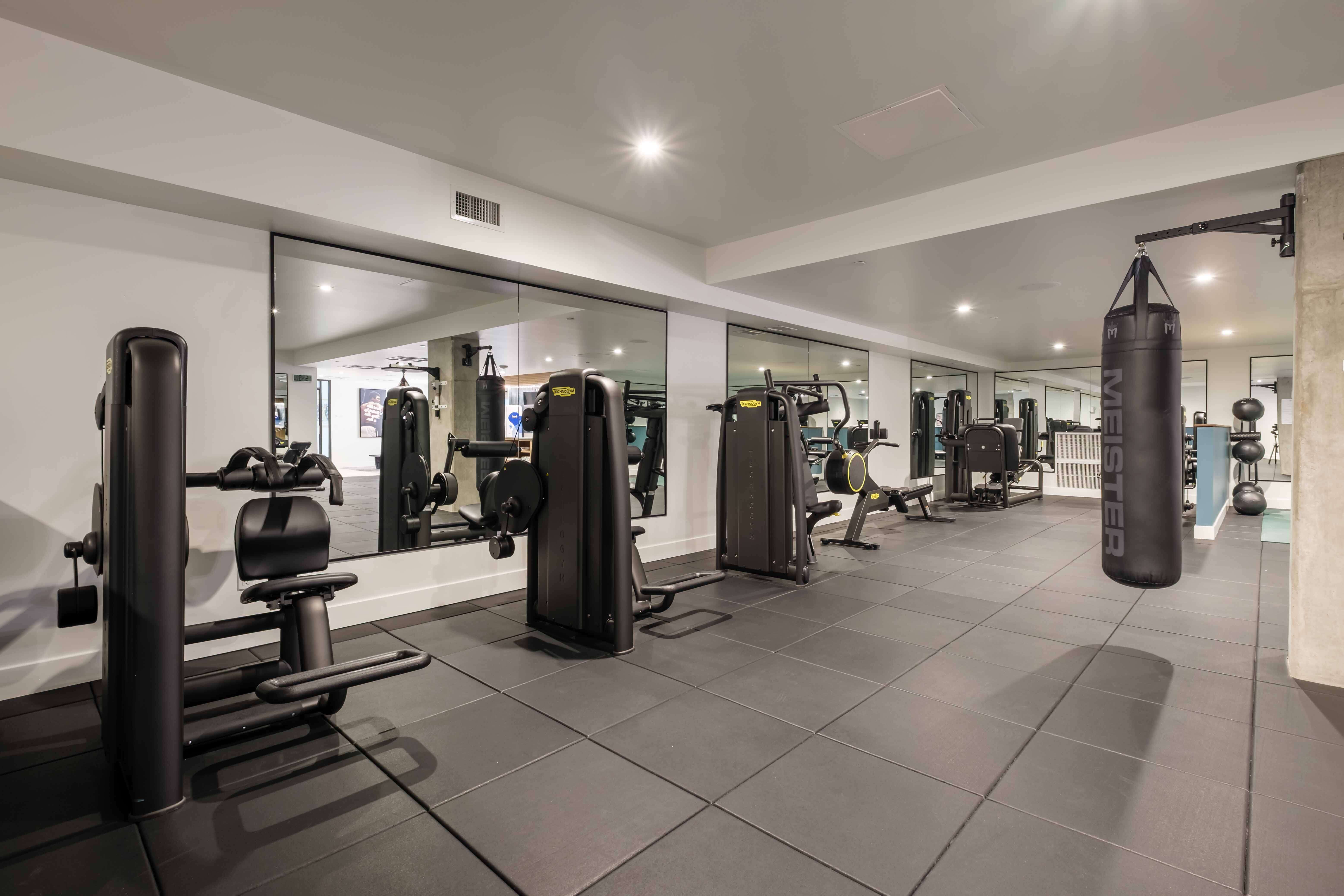 Modern gym room with black exercise machines, mirrors on the wall, and a hanging punching bag.