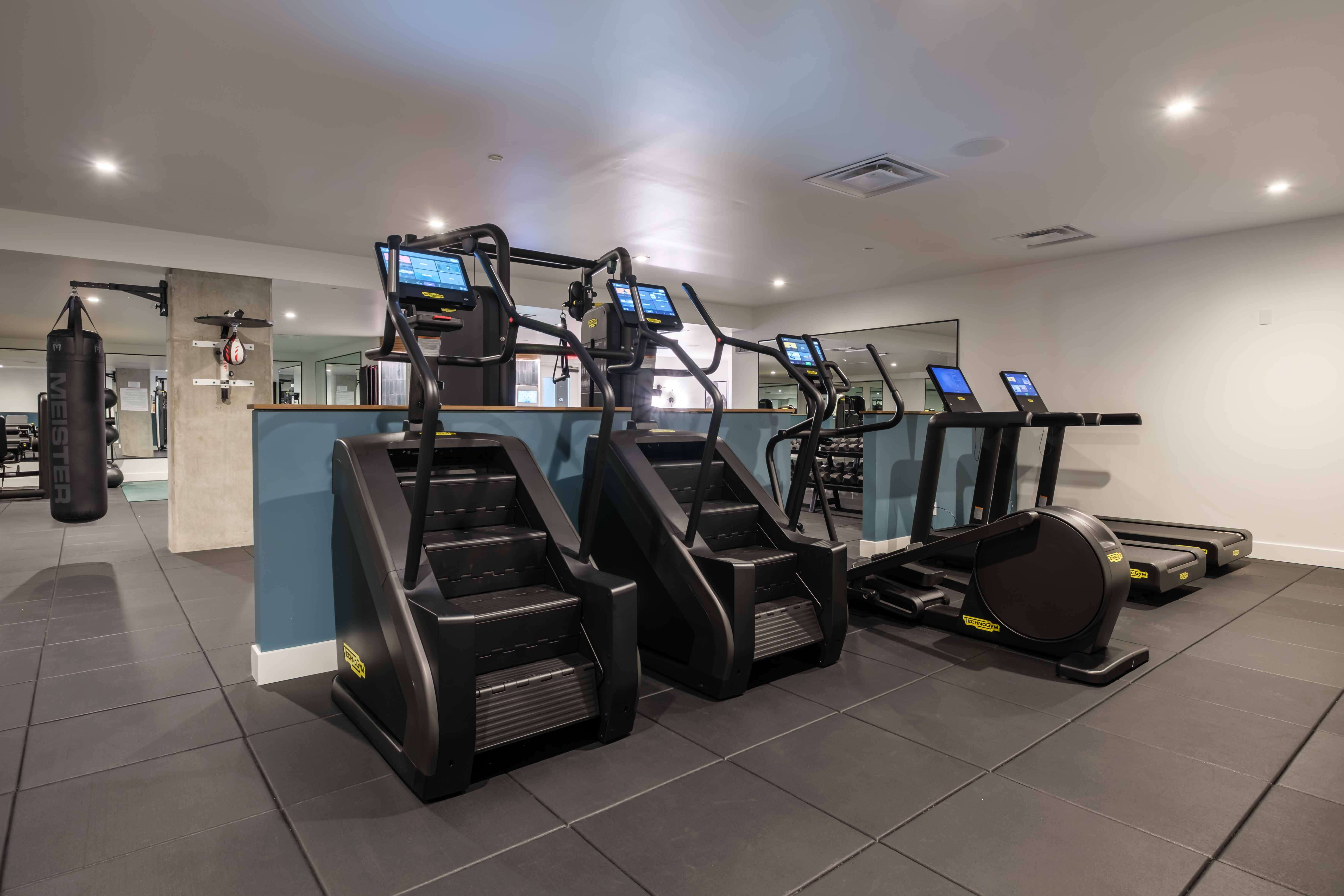 Modern gym with two stair climbers, two treadmills, and an elliptical machine on dark tiled floor.