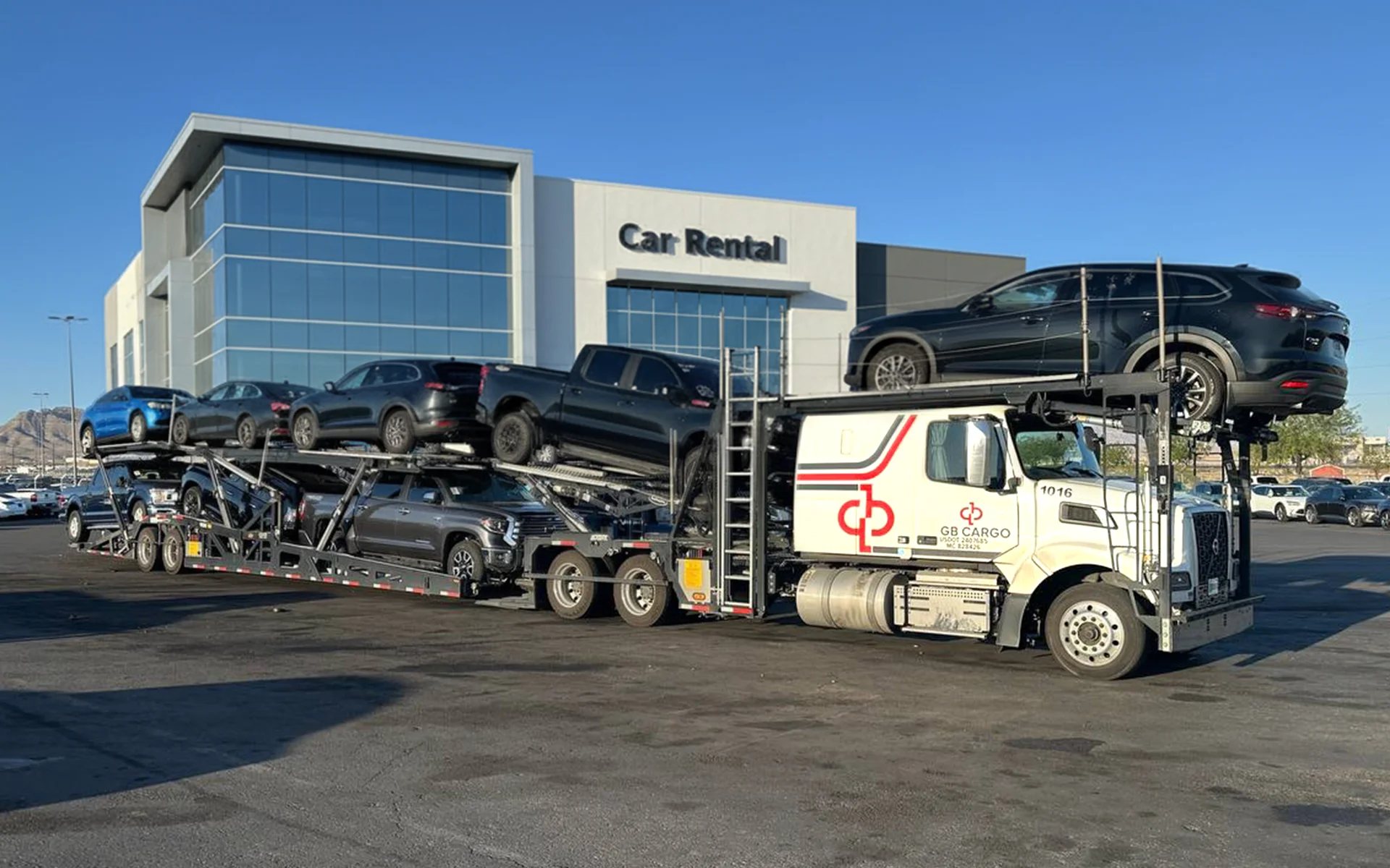 A GB Cargo's car hauling truck parked in front of car rental building.