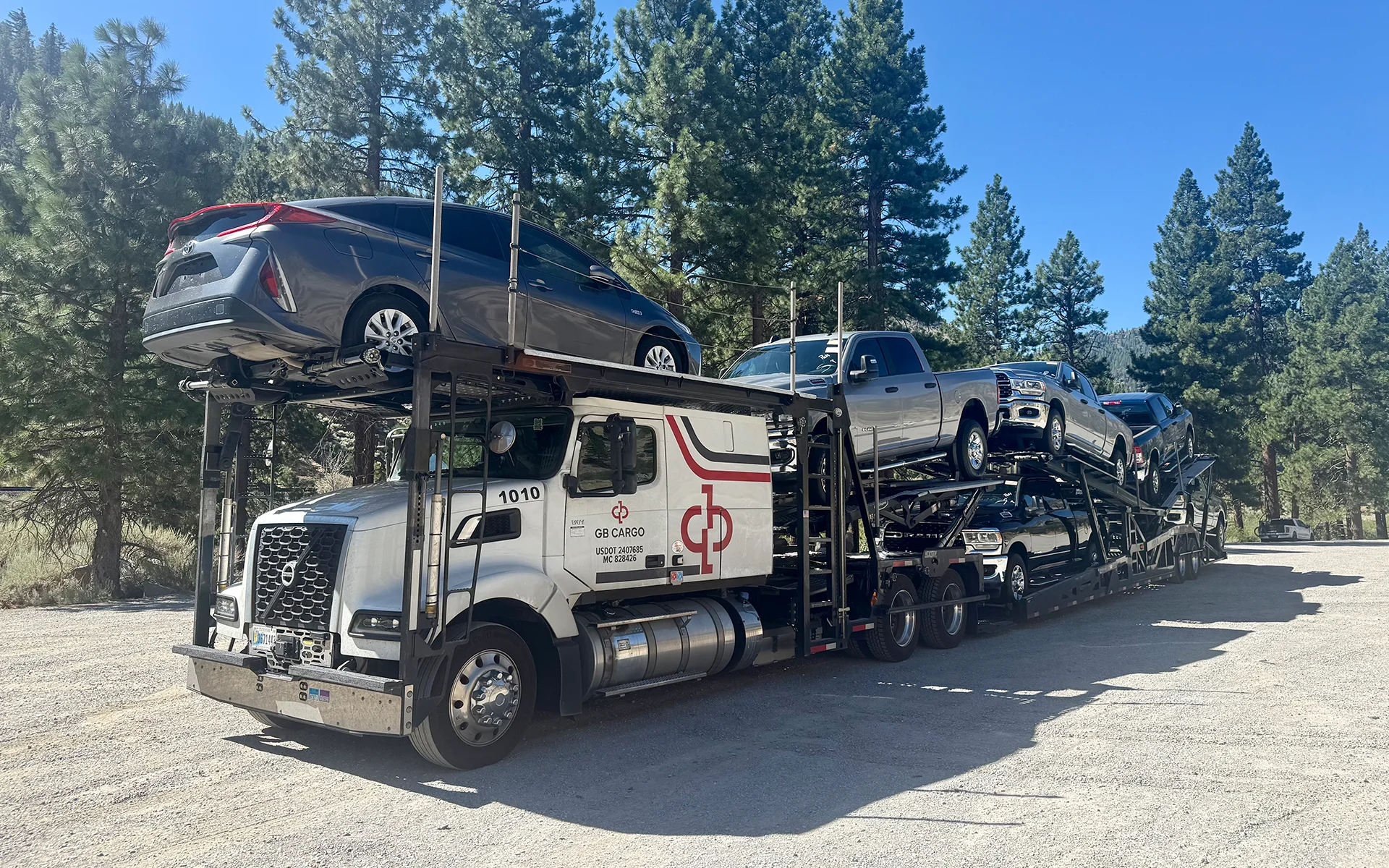 A GB Cargo's car hauling truck loaded with trucks parked on the side of the road.