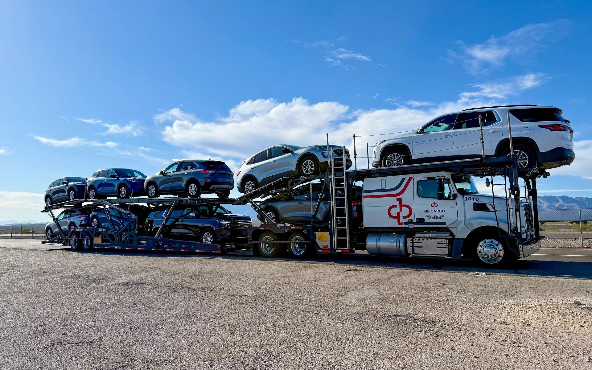 A GB Cargo car hauling truck loaded with cars parked on the side of the road.
