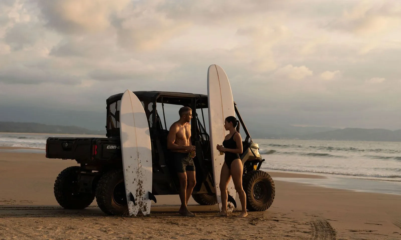 Man and woman at the beach with surfboards leaning against a Can-Am