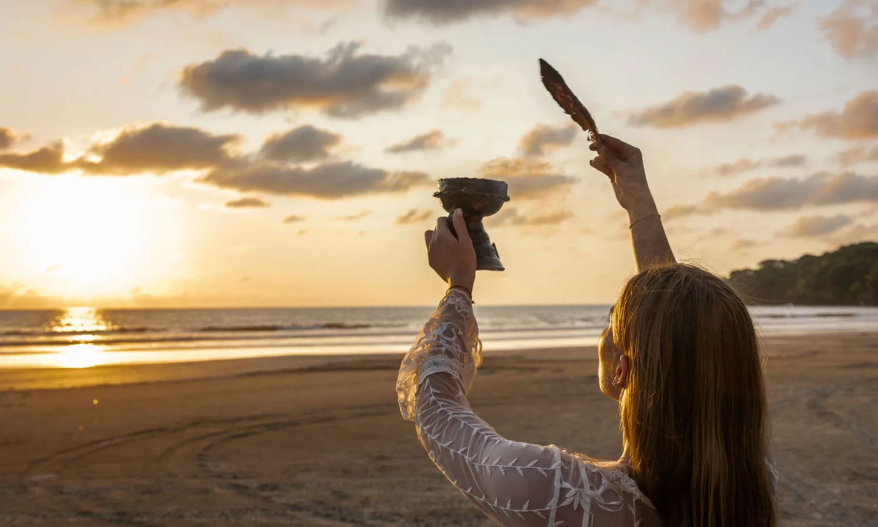 Young woman holding ceremonial chalice toward the sunset at the beach
