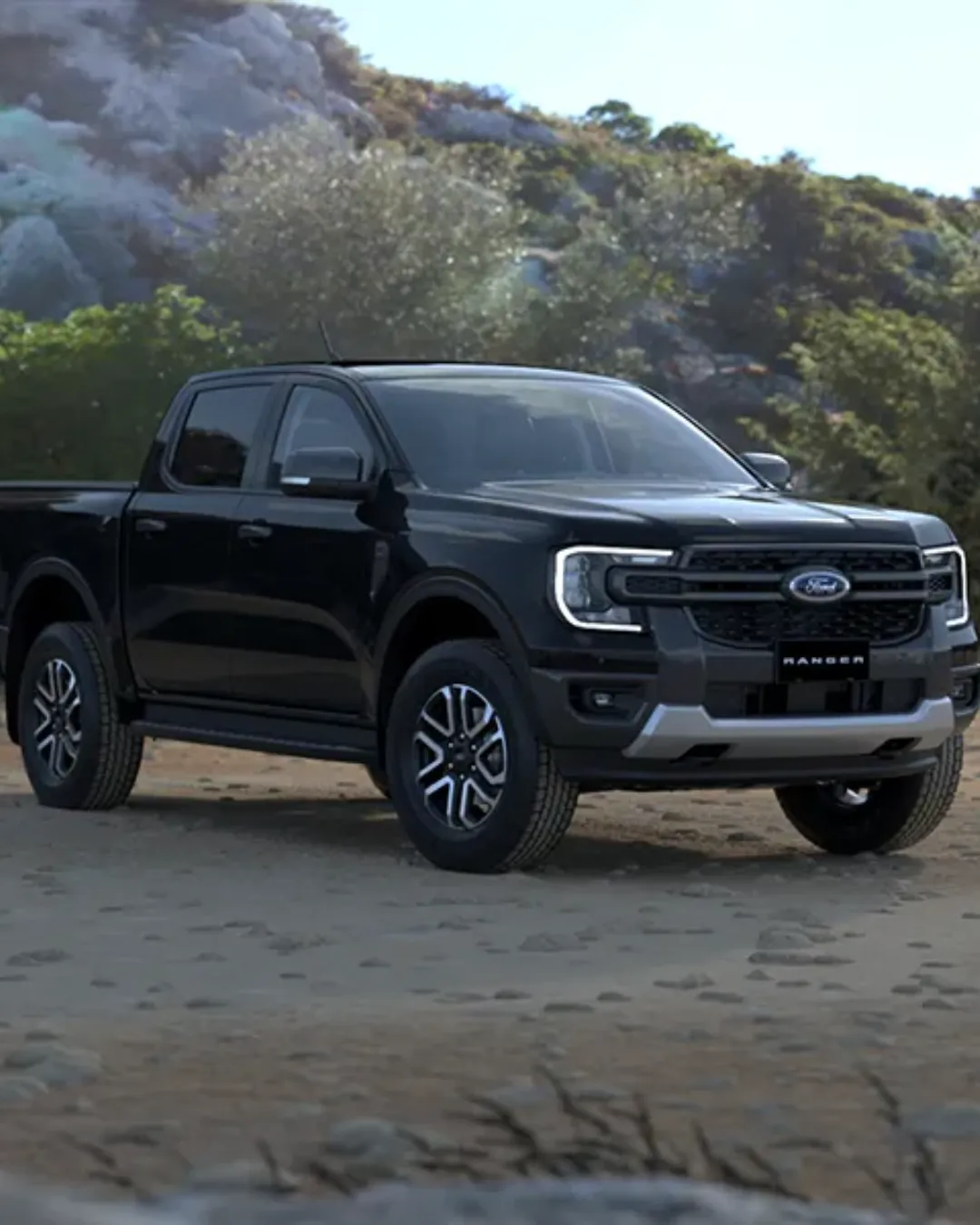 Black Ford Ranger double cab parked on a sandy track in front of a bush-covered hillside.