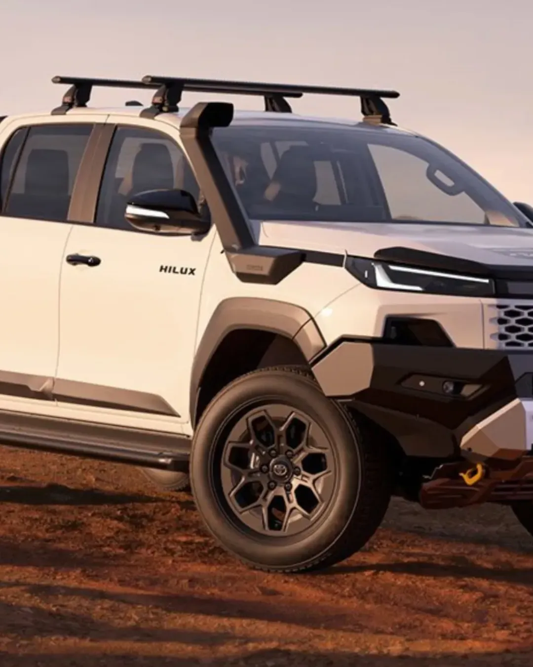 Cream Toyota Hilux with roof racks, a snorkel and a heavy-duty front bar, parked on red dirt at sunset.
