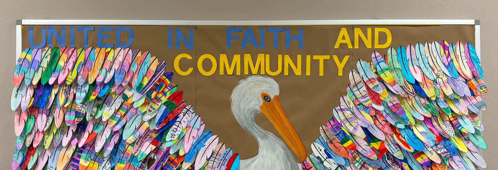 Colorful bulletin board with a pelican and the phrase 'UNITED IN FAITH AND COMMUNITY' surrounded by cut-out feathers decorated by different colors and patterns.