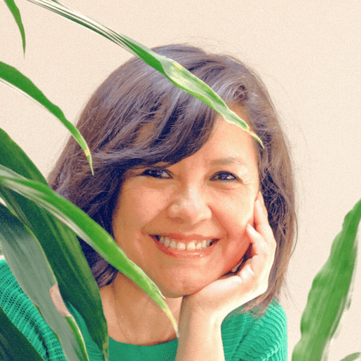 Cinthia Carvajal smiling in a close-up portrait, framed by lush green leaves.