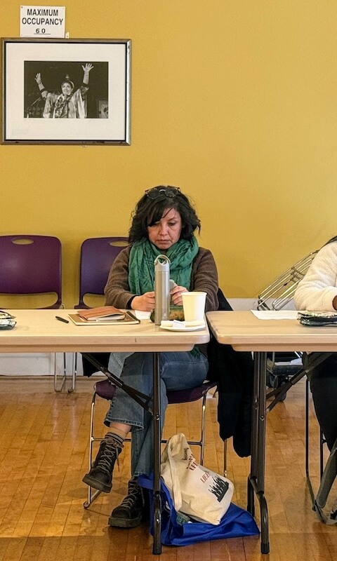 Cinthia Carvajal sits at a table during a meeting at The Women’s Building, focused on her notes with a warm scarf around her neck.
