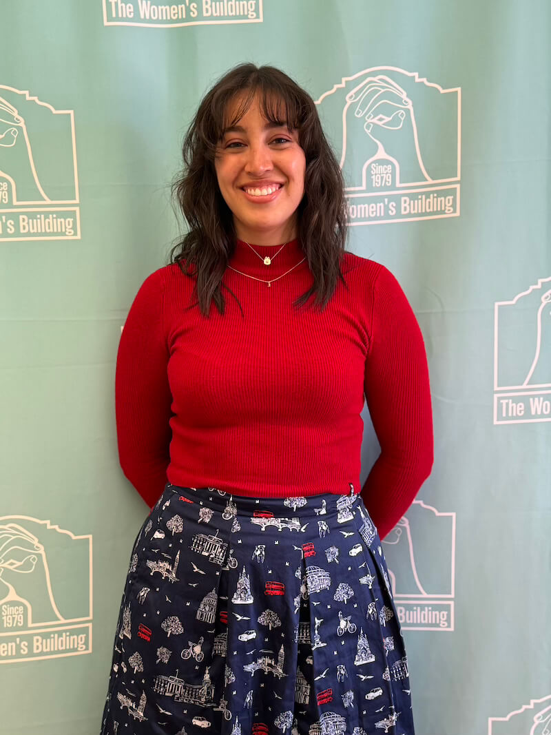 Valentina Ocampo Beltrán smiling in front of a teal Women’s Building backdrop while wearing a red top and patterned skirt.