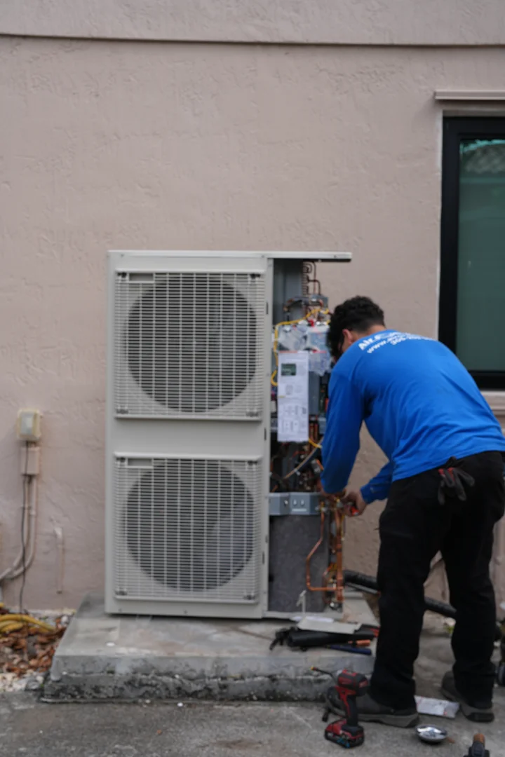 Technician inspecting an outdoor condenser in a sunny South Florida yard - ac tune up guide for south florida homeowners Technician inspecting an outdoor condenser in a sunny South Florida yard - ac tune up guide for south florida homeowners