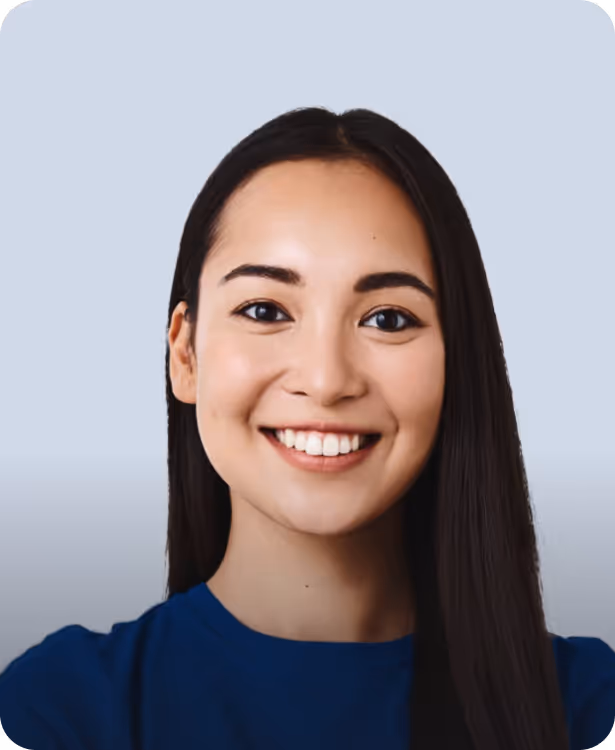 Smiling young woman with long dark hair wearing a blue top against a light gray background.