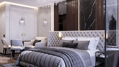 Modern bedroom with tufted gray bed, gray bedding, two wall-mounted lamps, and dining area with round table and chairs.