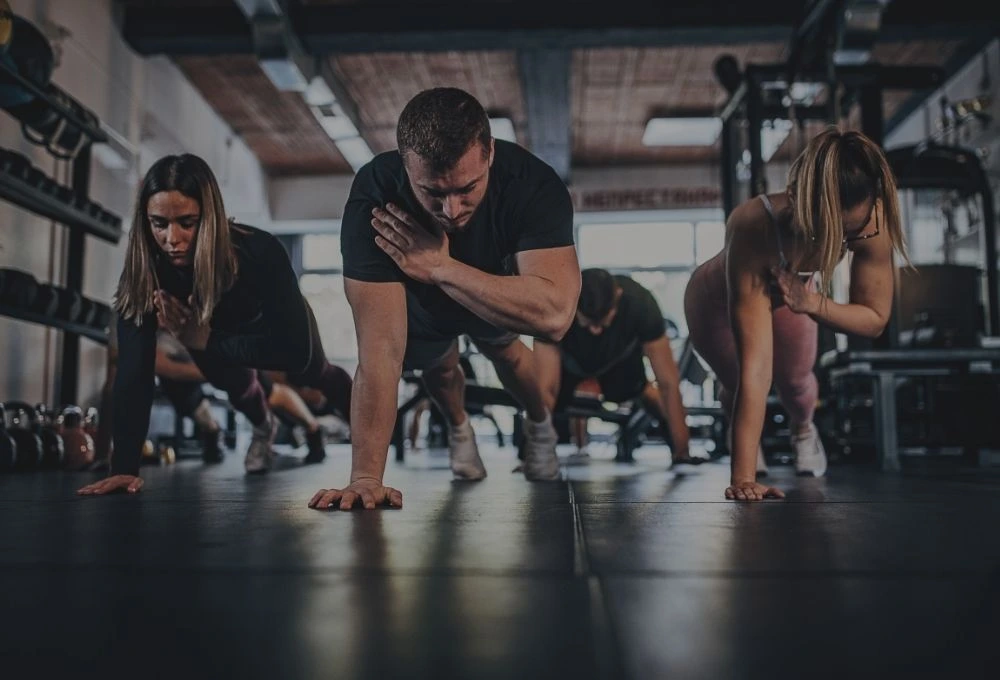 En man och två kvinnor som tränar och står i en hög plankposition och sträcker höger handen mot vänster axel.