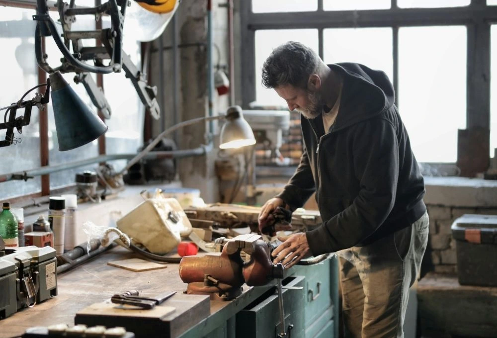 En man ståendes i en vid en bänk i verkstad arbetandes med ett projekt.