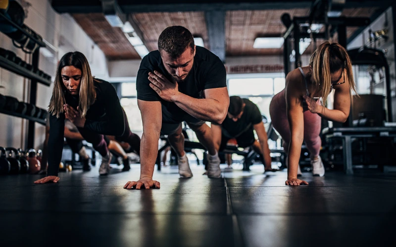 En man och två kvinnor som tränar och står i en hög plankposition och sträcker höger handen mot vänster axel.