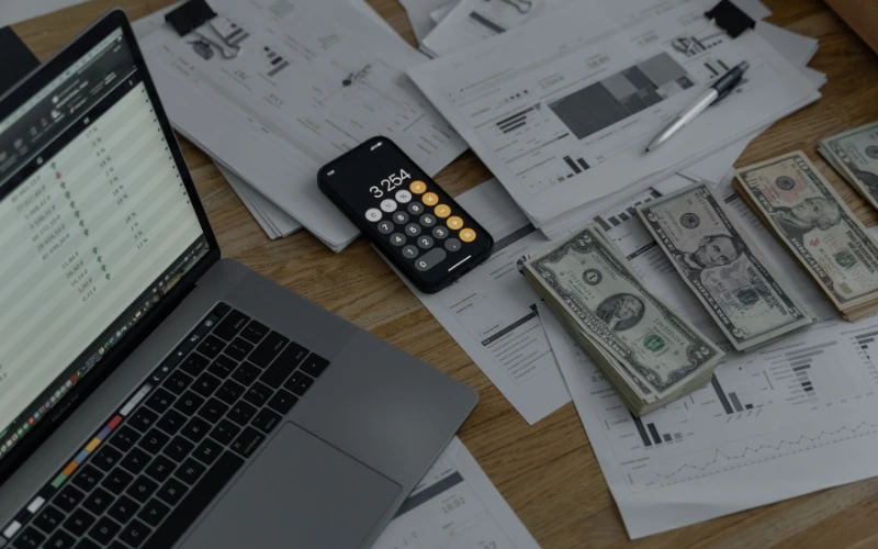 Papper, en dator och pengar på ett träbord 