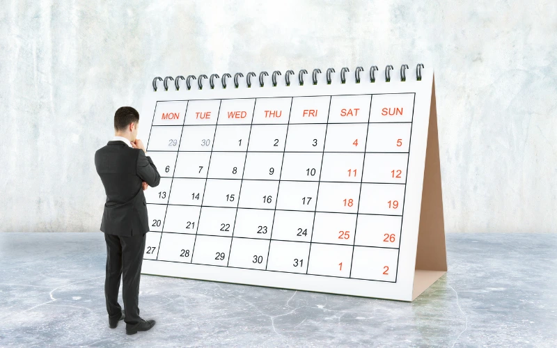 En man i svartkostym ståendes framför en gigantisk kalender med ryggen vänd mot kameran.