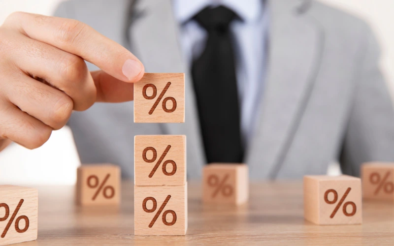 En man i gråkostym och slips syns bakom staplar tre träkuber med en procentsymbol på höjden. 