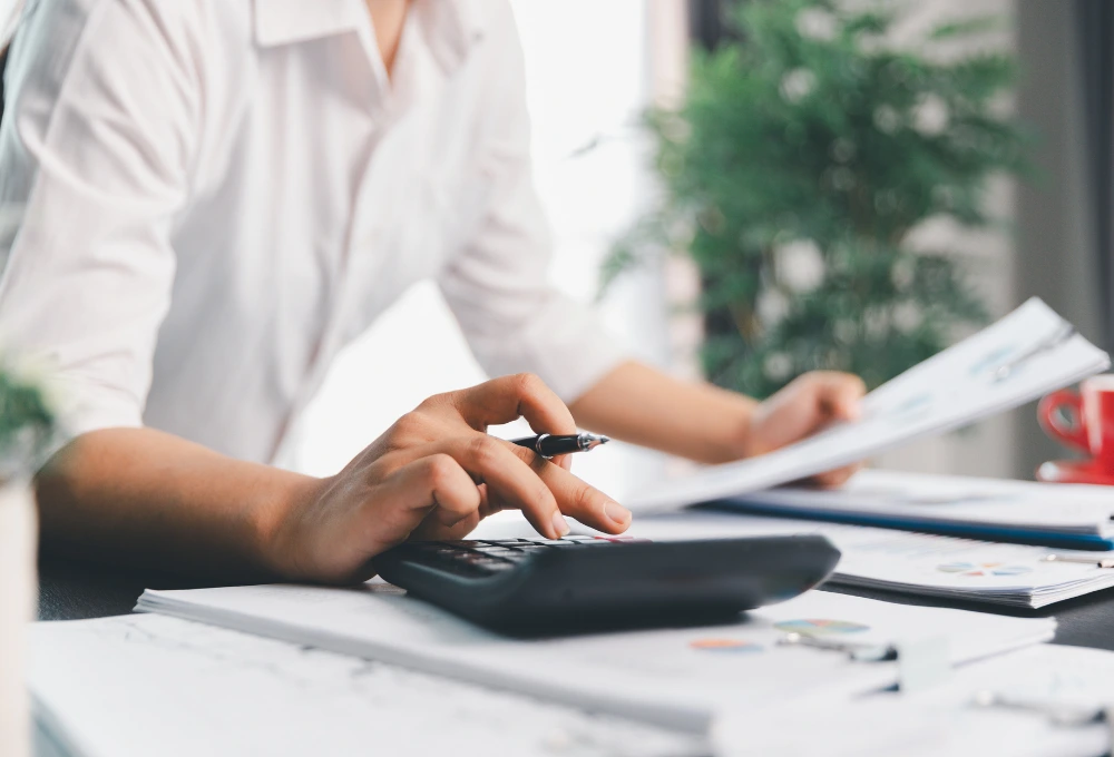 En person iklädd vit skjorta sitter och jobbar där man ser handen trycka på en vit miniräknare.