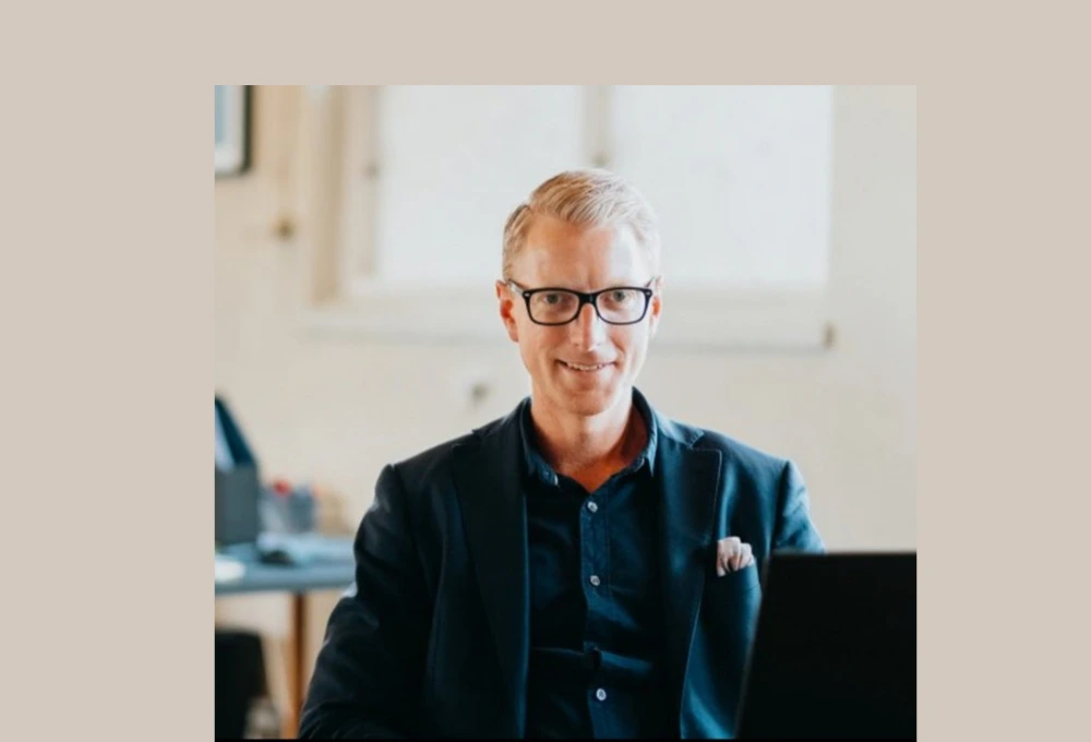 Bild på David sittandes i en kontorslokal i klädd en mörk kostym.