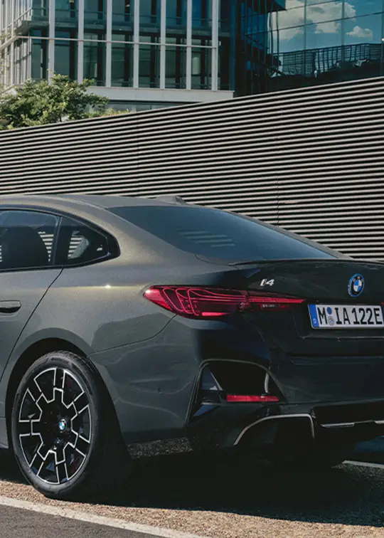 BMW i4 in mattem Grau beim Laden an moderner E-Ladesäule vor urbaner Glasarchitektur – BMW Köhler in Karlstadt