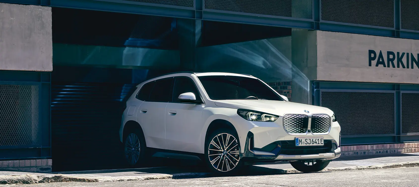 Weißer BMW iX1 SUV mit markanter Front fährt aus einer Tiefgarage ins Sonnenlicht – BMW Köhler in Karlstadt