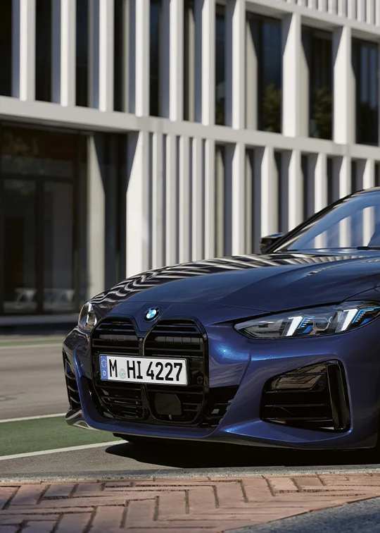 BMW i4 in Blau auf urbaner Straße mit moderner Architektur im Hintergrund – BMW Köhler in Karlstadt