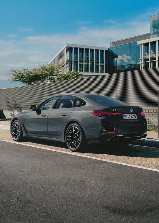 BMW i4 in mattem Grau beim Laden an moderner Ladesäule vor urbanem Bürogebäude – BMW Köhler in Karlstadt