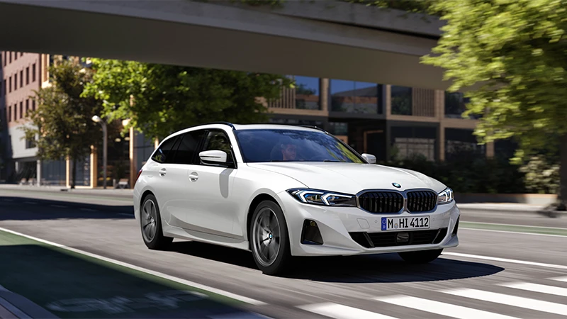 Weißer BMW 3er Touring in Bewegung auf urbaner Straße unter moderner Architektur – BMW Köhler in Karlstadt