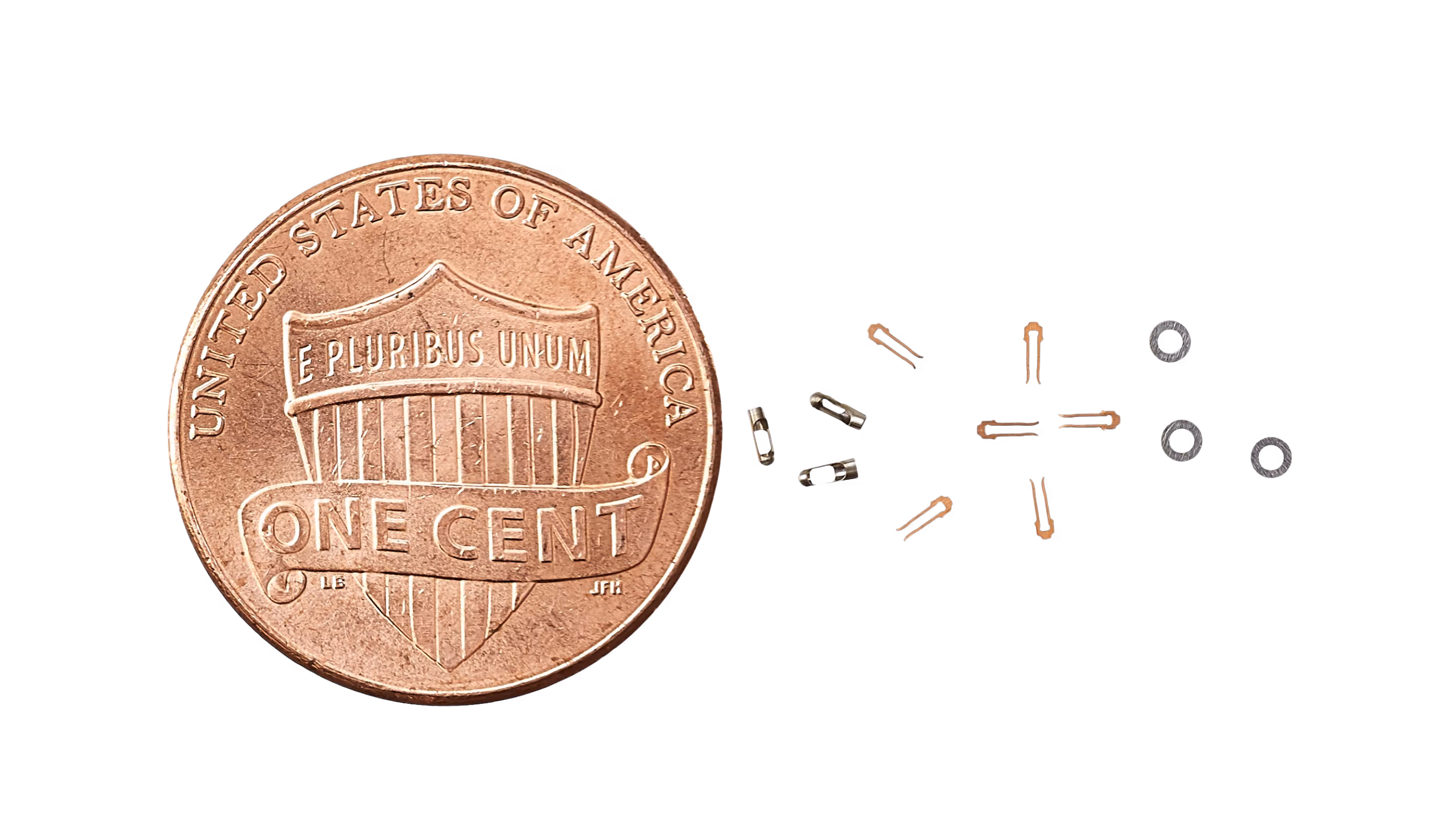 Precision metal cut components next to a penny for size comparison