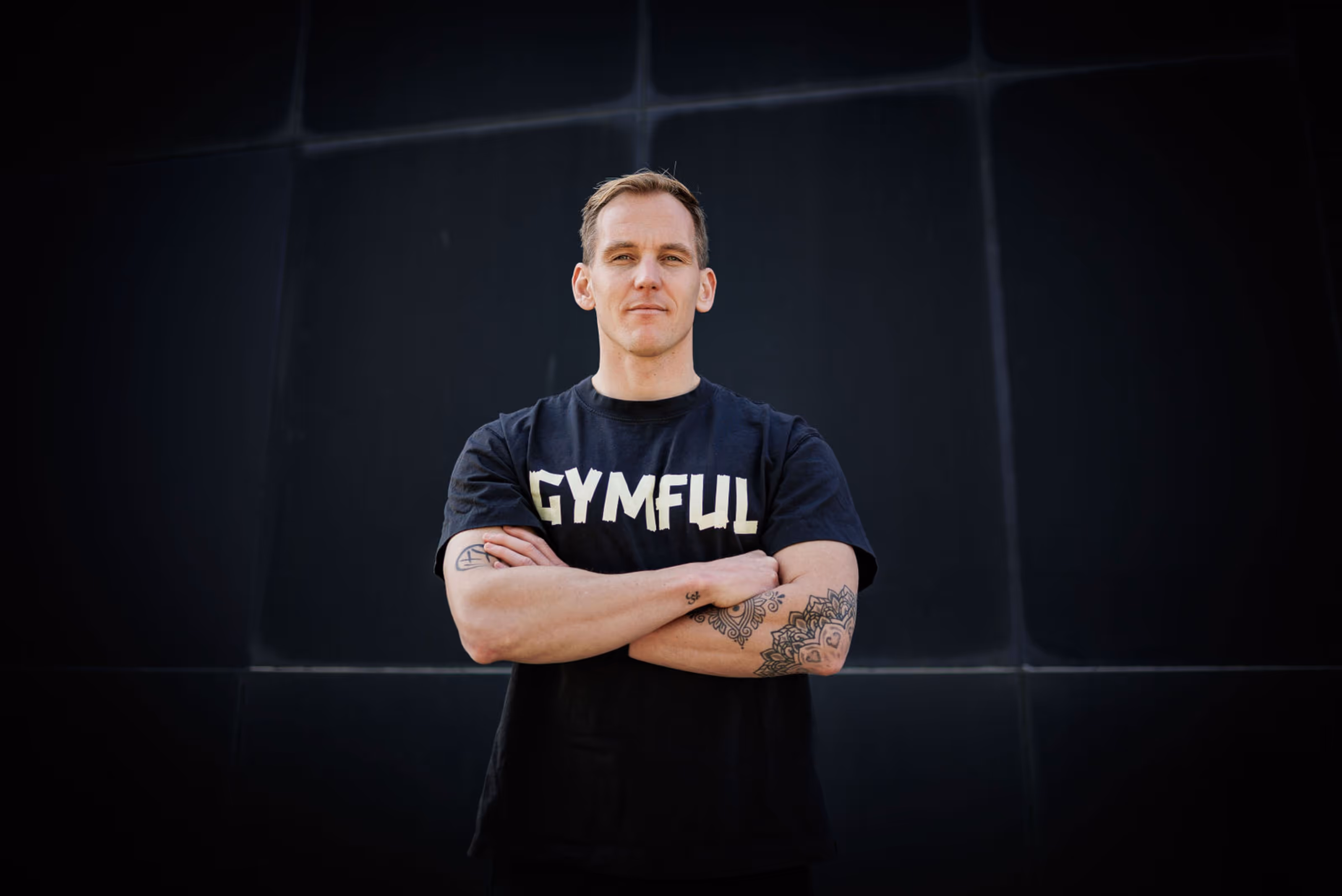 Sebastian Smeenk, eigenaar van Gymful staat geposeerd voor een zwarte achtergrond met zijn armen over elkaar gekruist en draagt een t-shirt met daarop "Gymful"
