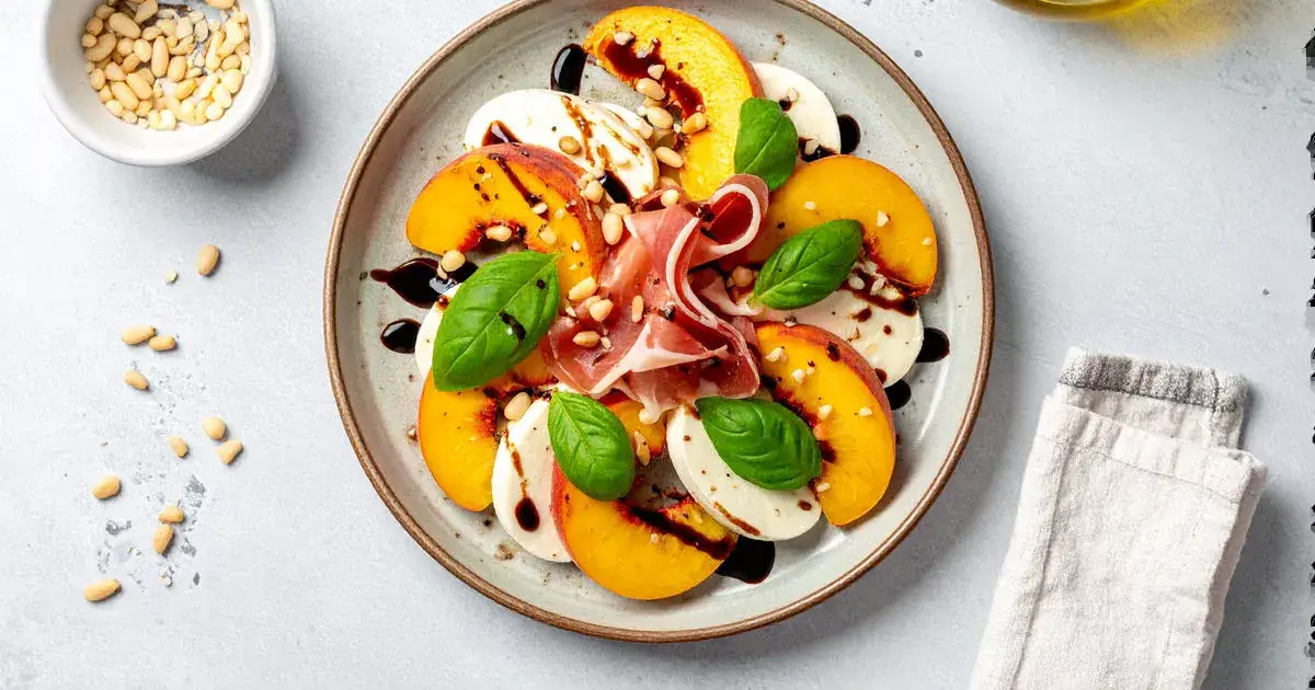 Caprese-Salat mit Pfirsich, Mozzarella und Prosciutto auf einem Teller angerichtet