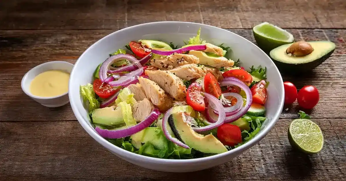 Avocado-Hähnchen-Salat mit Limetten-Dressing, serviert in einer Schüssel, garniert mit frischen Zutaten und Limettenspalten