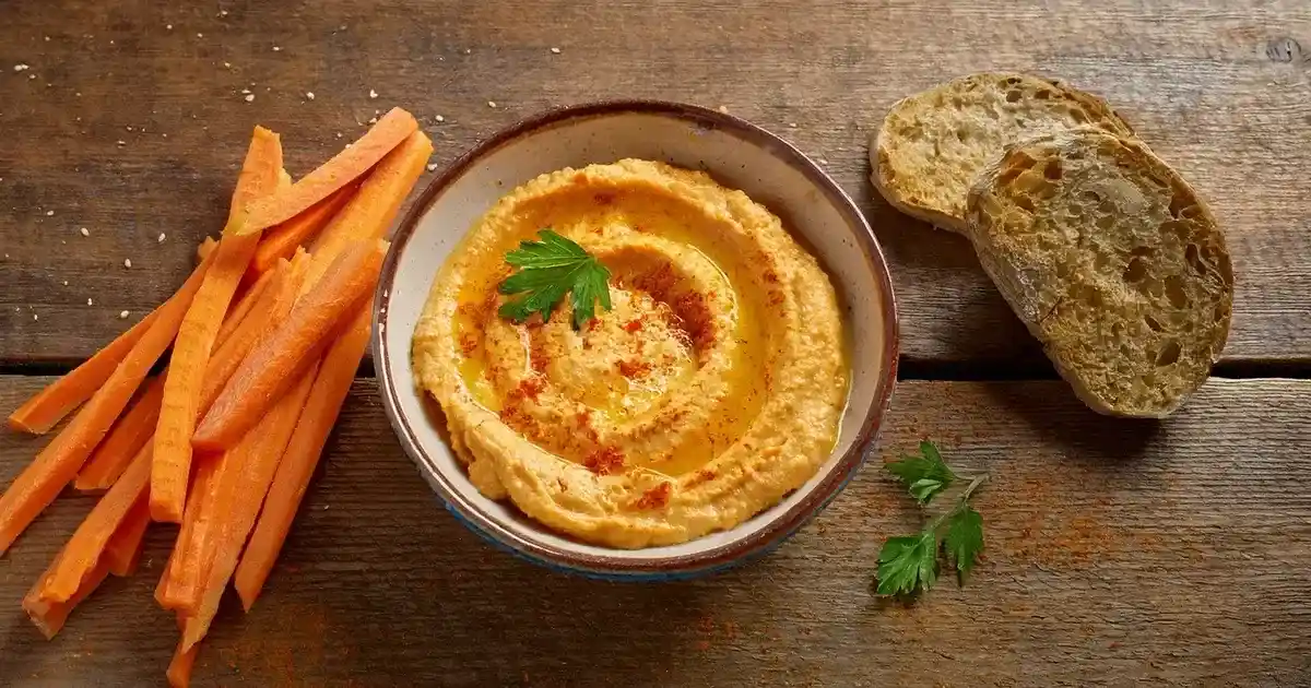 Cremiger Karotten-Hummus mit Olivenöl und Gewürzen serviert
