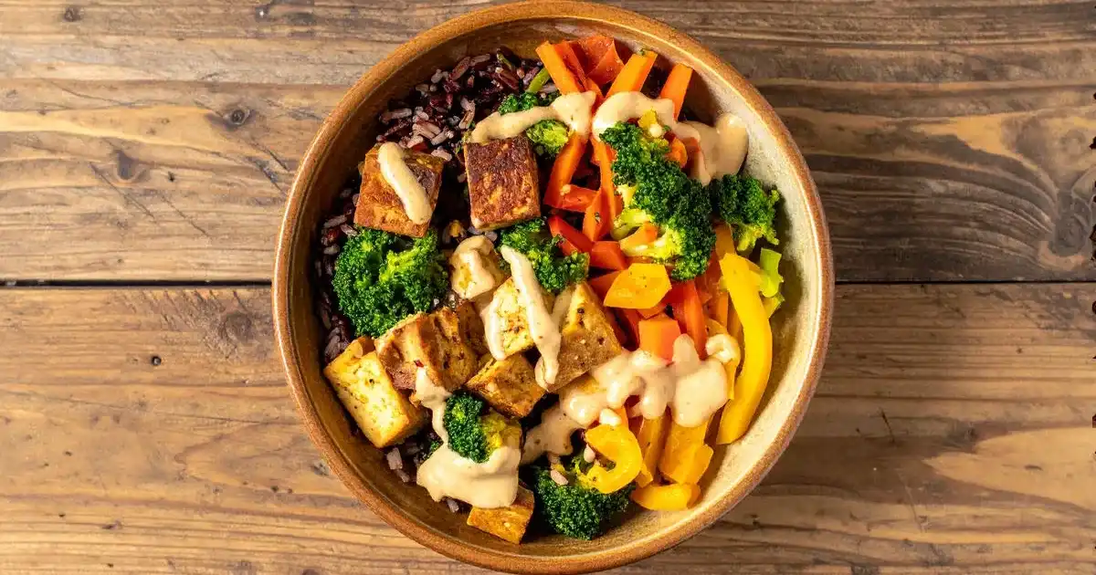 Tempeh-Bowl mit Wildreis, gebratenem Tempeh, Gemüse und Erdnusssoße in einer rustikalen Schale.
