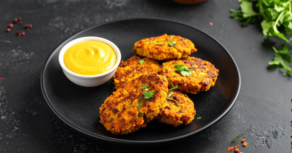 Linsen-Möhren-Bratlinge mit Curry-Dip auf einem dunklen Teller